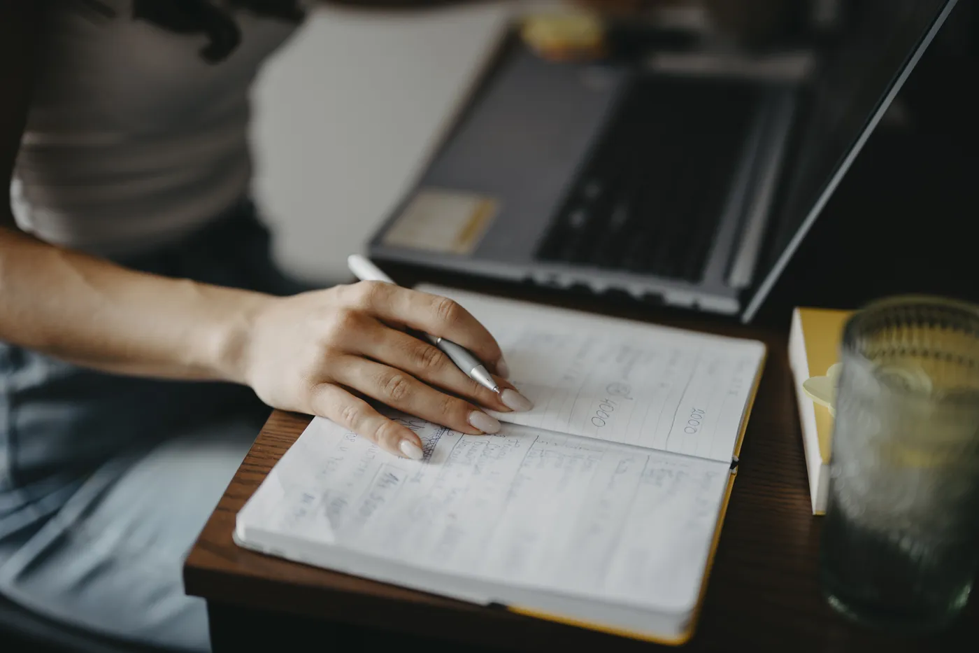 Writing research notes in a notebook beside a laptop